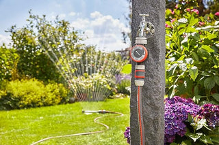 Gardena water timer on a garden faucet while a sprinkler waters the lawn