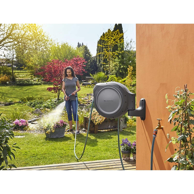 Gardener watering flowers with hose from the Gardena wall reel