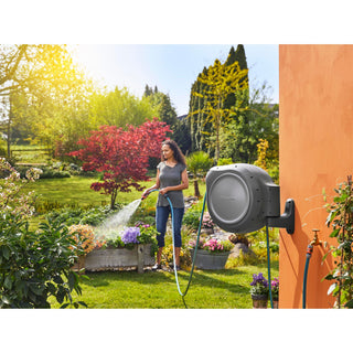 Gardener watering flower beds with hose from the wall-mounted Gardena reel