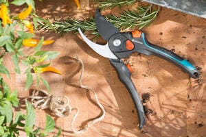 Gardena pruners on a wooden table with rosemary, chili peppers and twine