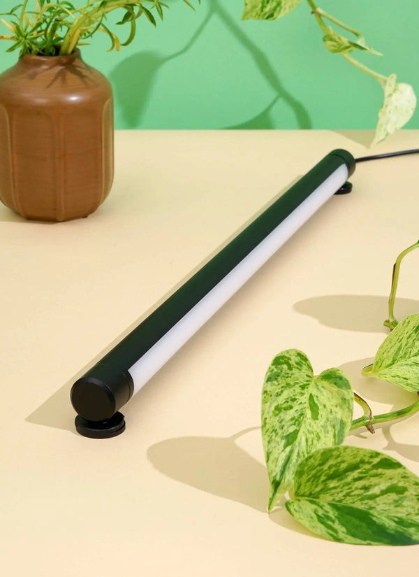 Soltech Grove LED grow light bar in black lying on a table beside potted plants