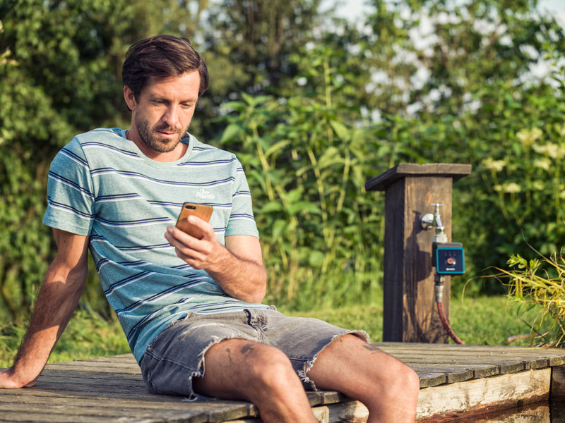 Gardener on a deck setting the Gardena Bluetooth timer on a garden post from a phone