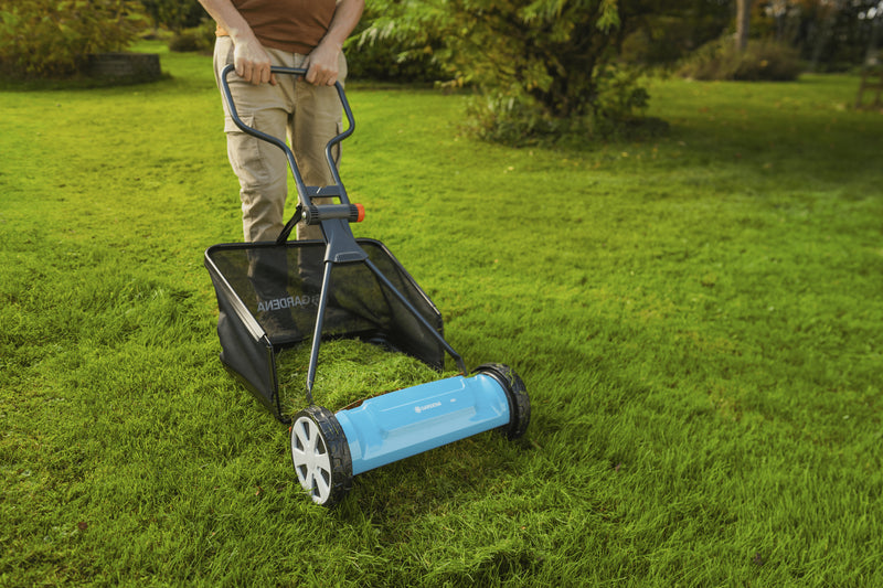Man mowing a lawn with the grass catcher fitted to a Gardena reel mower