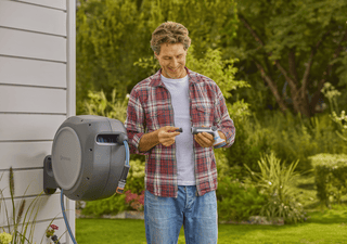 Gardener holding a spray nozzle beside the wall-mounted Gardena reel